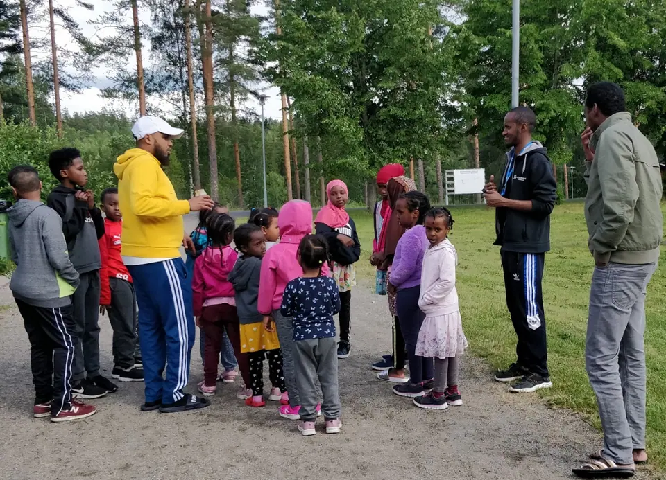 Lapset ja aikuiset viettävät aikaa yhdessä metsäisellä retkipaikalla.
