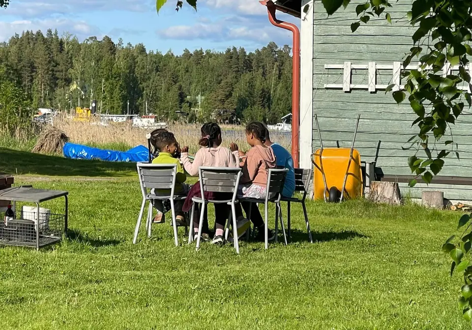 Osallistujat kokoontuvat pöydän ääreen kesäisessä pihapiirissä.